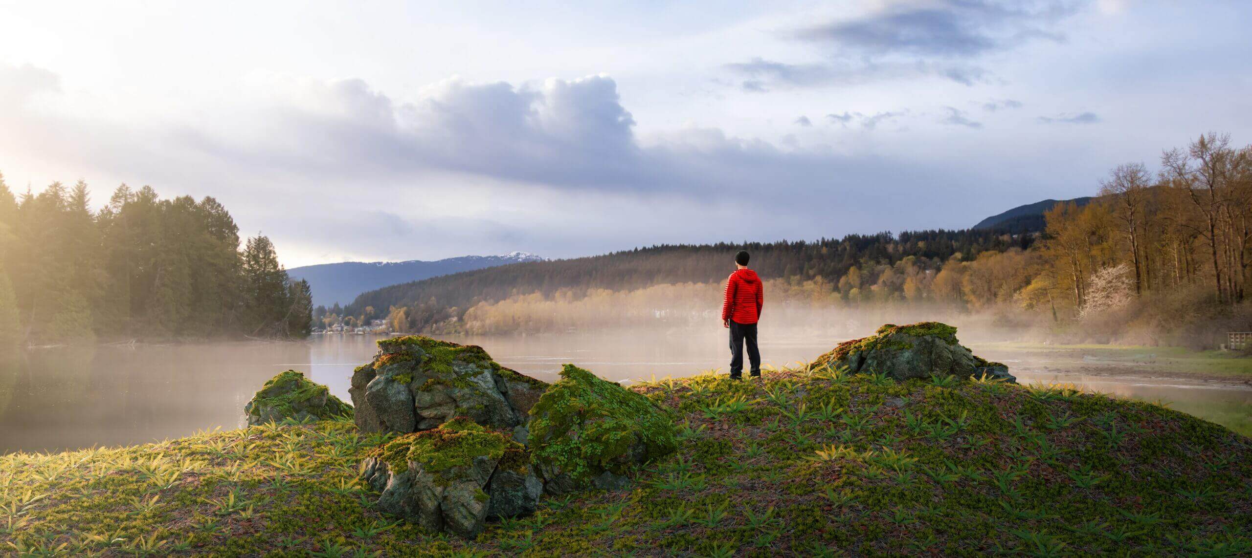 Man in red jacket overlooking misty lake