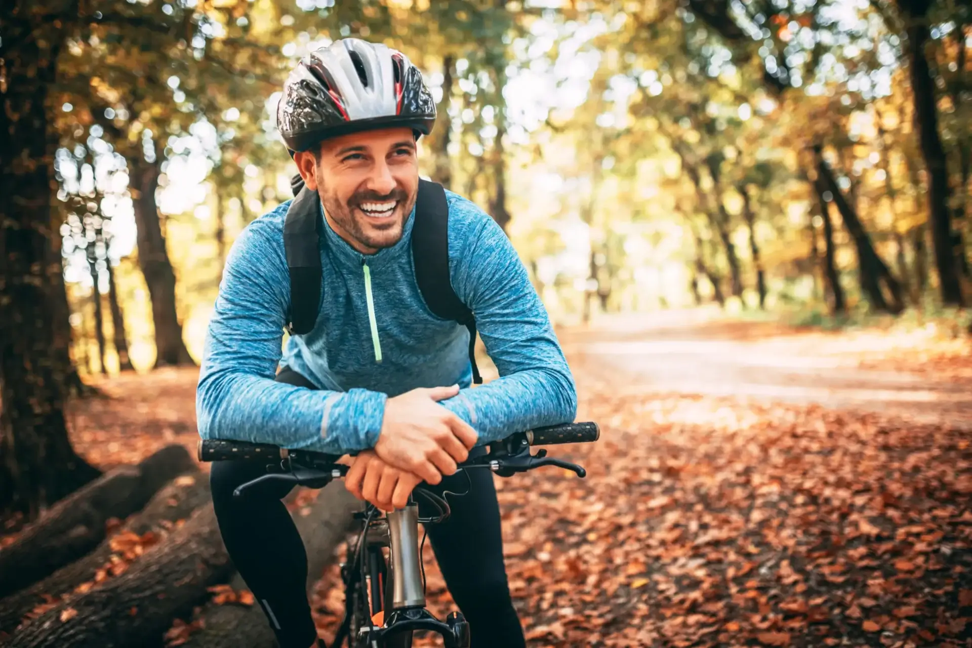 Happy biker leaning on handlebars amid leaves